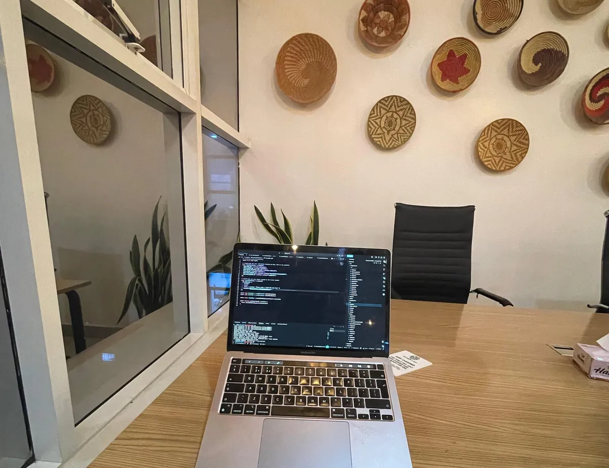 A laptop open on a wooden desk, with woven baskets on the wall behind it
